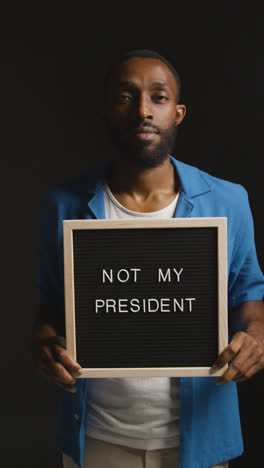 Vertical-Video-Portrait-Of-Vertical-Video-Shot-Of-Man-Holding-Not-My-President-Sign-In-Election-Against-Black-Background